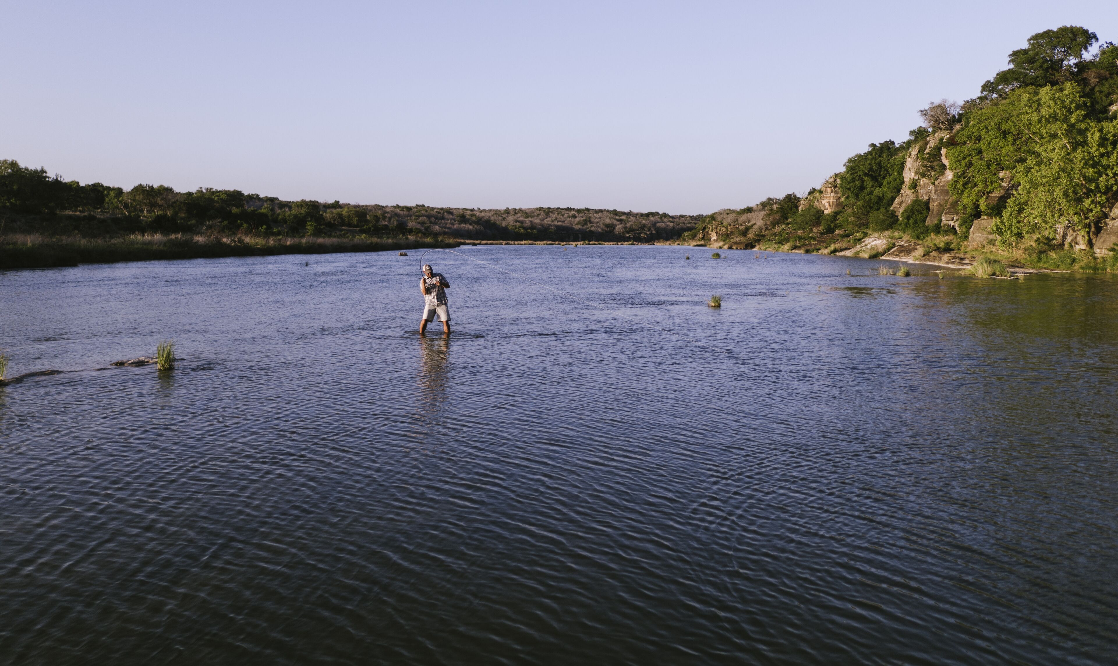 Une personne qui marche dans l’eau d’une rivière paisible, entourée d’un paysage naturel.