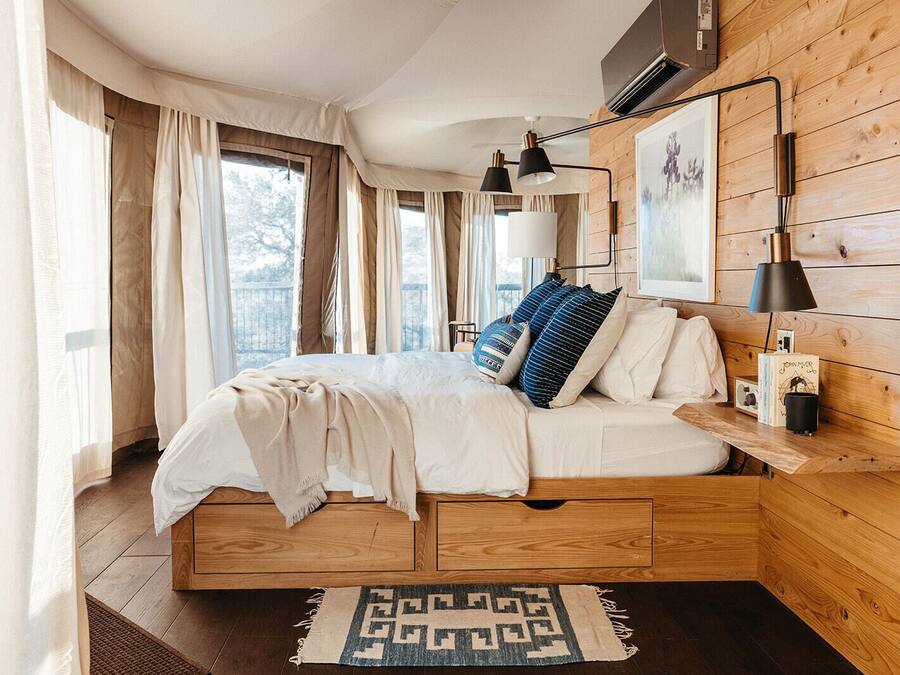 A bedroom with a wooden bed frame, a bedside table with a lamp, and a window with curtains.