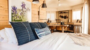 Un dormitorio con una cama grande, cabecera de madera, un cuadro de flores, un escritorio y una kitchenette.