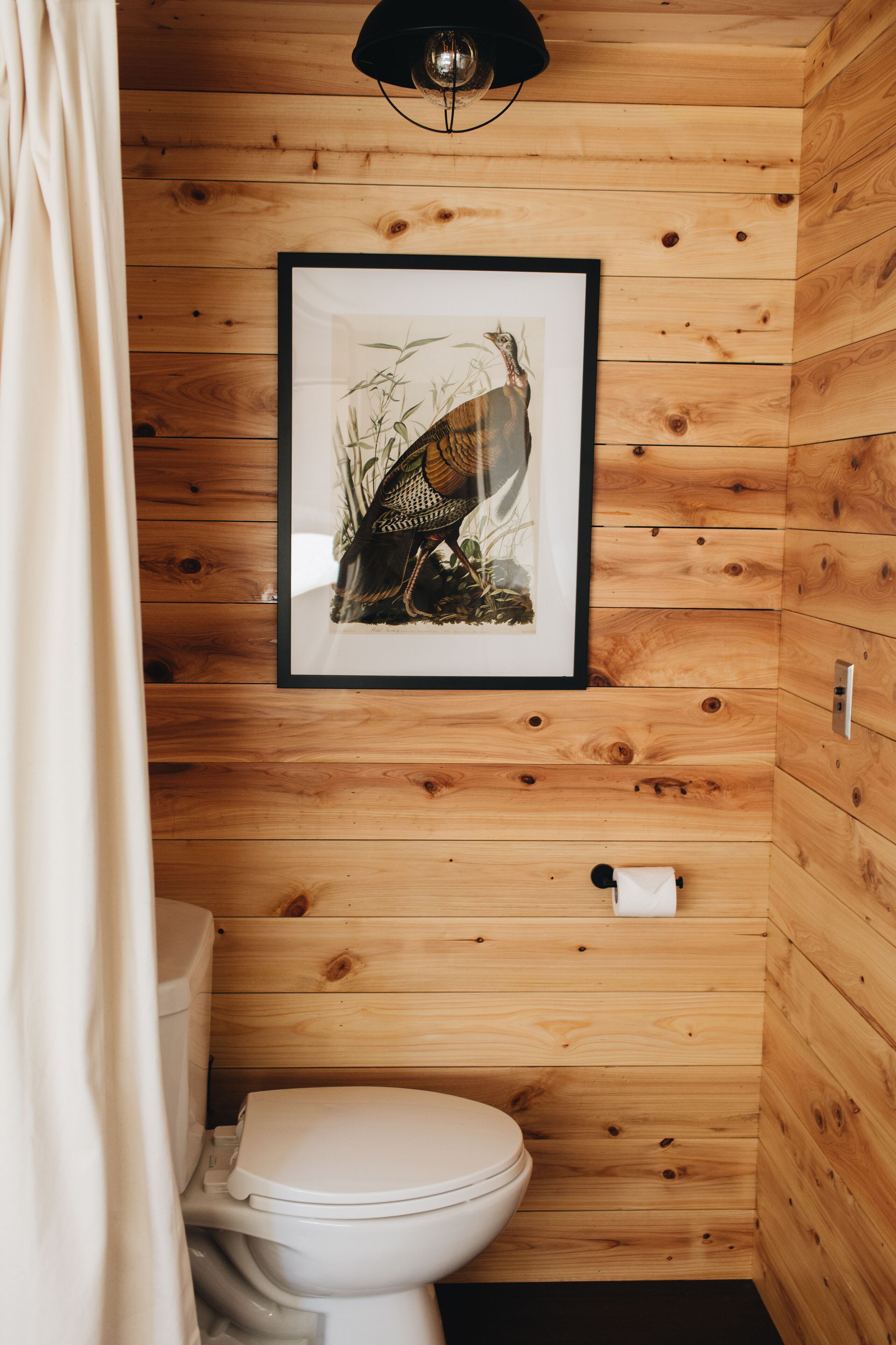 A wooden-paneled bathroom with a framed picture on the wall, a toilet, and a towel dispenser.