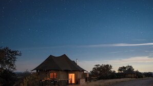 Una casa con techo de paja, un porche y vista al cielo nocturno.
