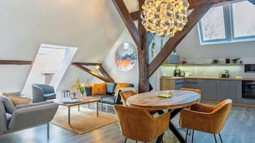 A modern loft with exposed wooden beams, a dining area with a wooden table and chairs, a kitchen with a view, and a living area with a sofa and coffee table.