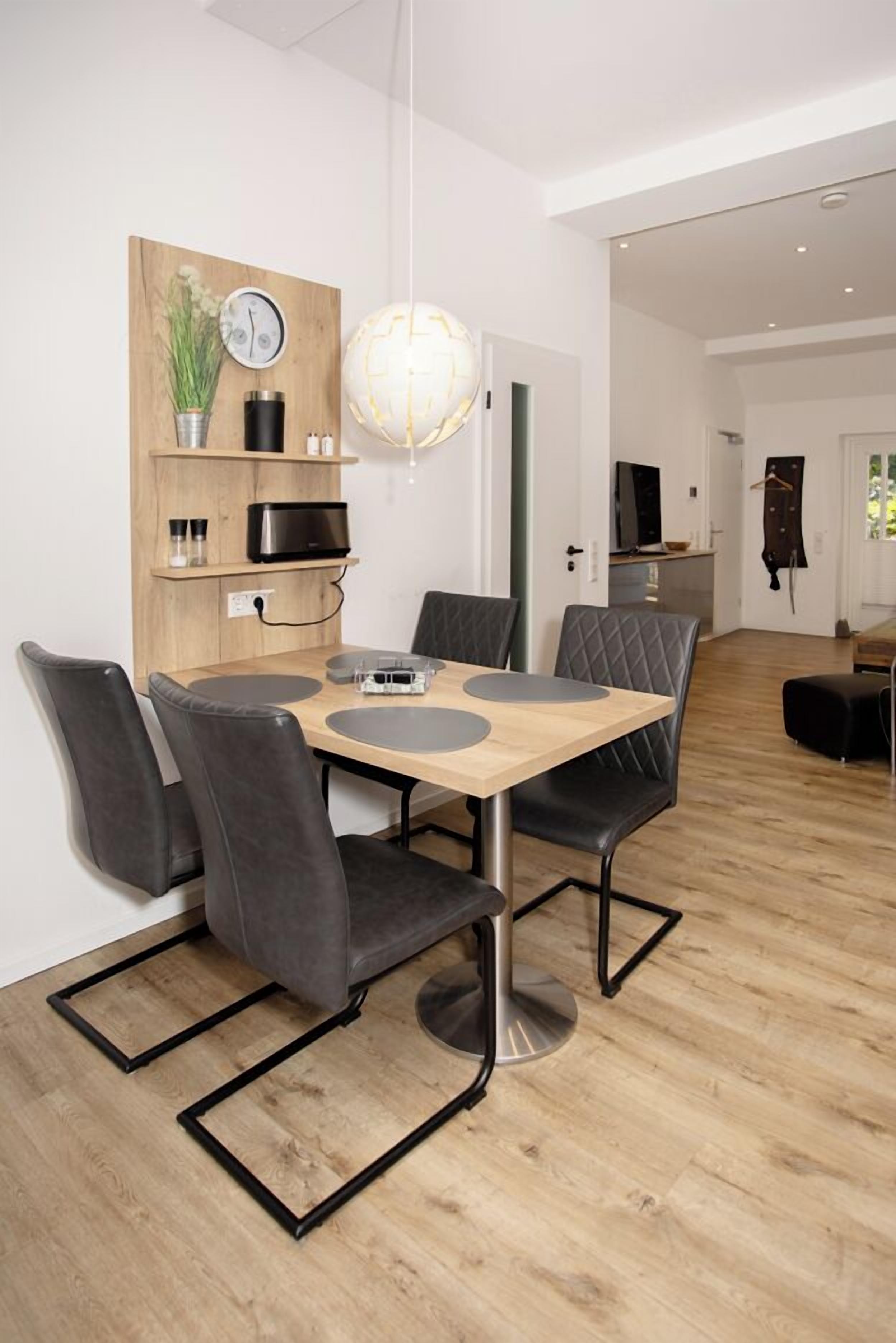A modern dining area with a wooden table, black chairs, and a pendant light.