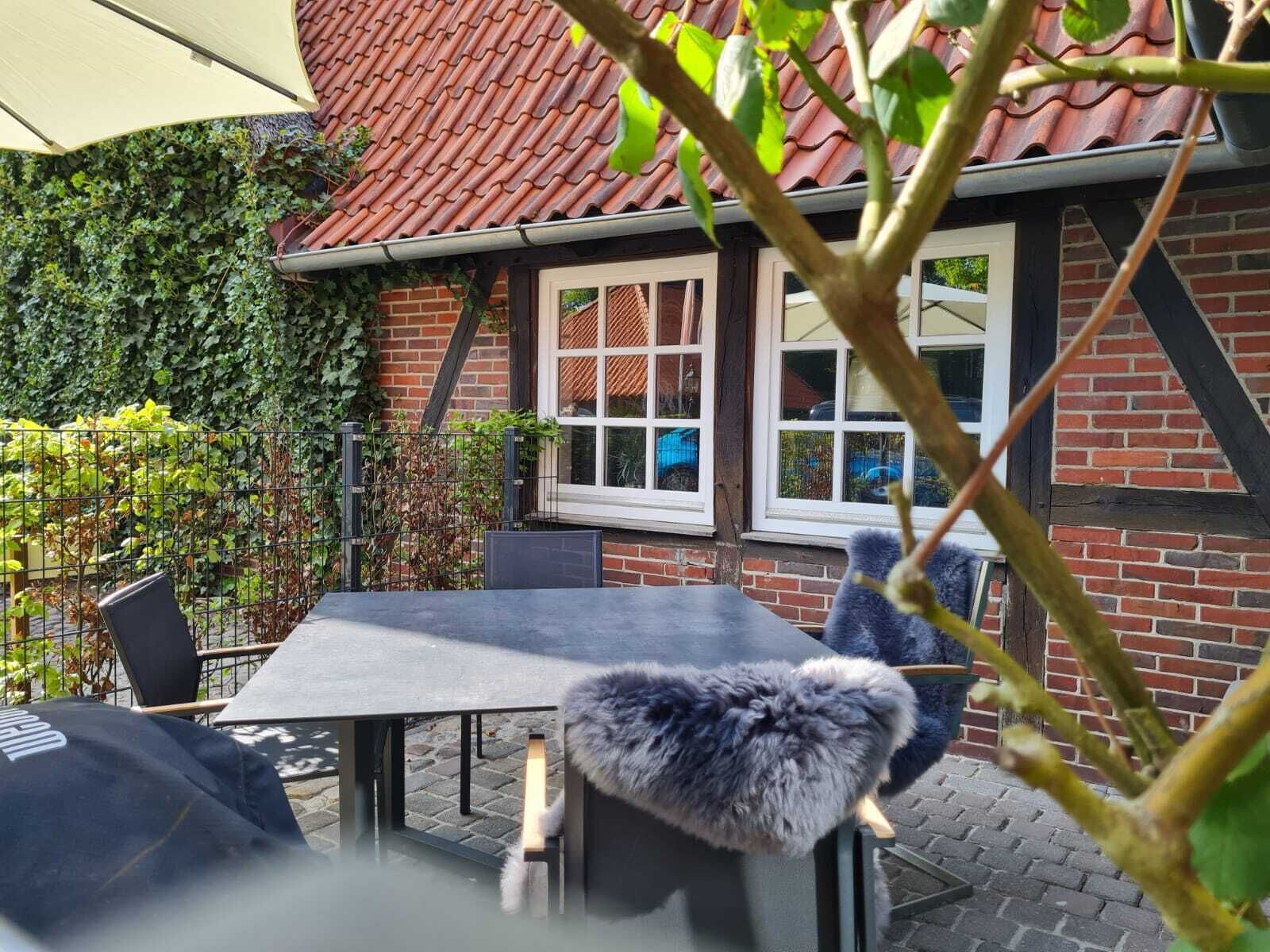 An outdoor patio area with a table and chairs, a brick building with a red-tiled roof, and a view of the street.