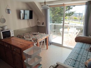 A cozy living space with a dining table, a sofa, a TV mounted on the wall, and a balcony with a view of the outdoors.