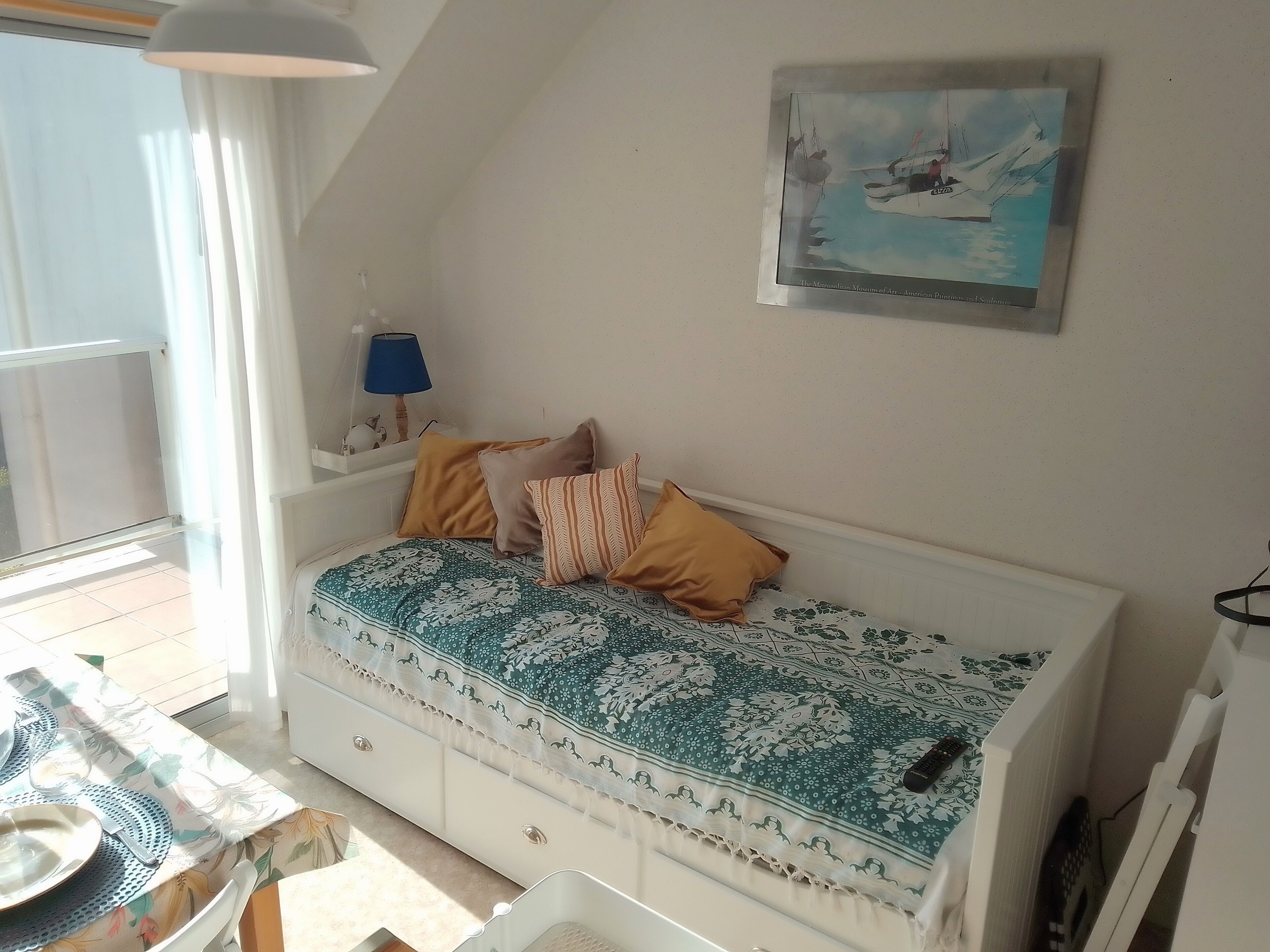 Una habitación acogedora con una cama, un cuadro, una lámpara y una mesa dispuesta para comer.