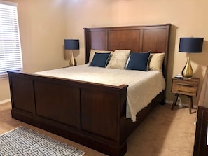 Quarto com uma cama de madeira grande, duas mesas de cabeceira com luminárias, um tapete estampado e uma janela com persianas.
