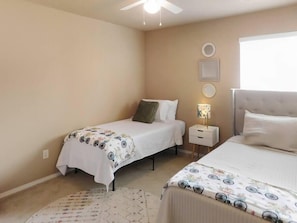 Une chambre avec deux lits, un ventilateur de plafond, une table de chevet avec une lampe et une fenêtre.