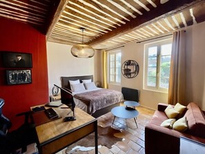 A room with a bed, a desk, a chair, a sofa, and a large window.