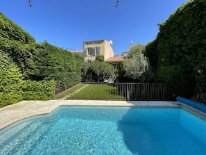 A swimming pool with a clear blue water, surrounded by lush greenery and a fence.