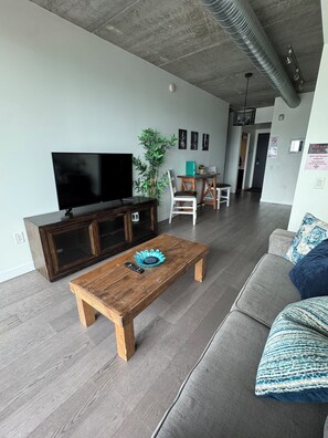 Un salon moderne dotĂ© dâun tĂ©lĂ©viseur Ă Ă©cran plat, dâune table basse en bois, dâun canapĂ© gris et dâun coin repas avec une table et des chaises.