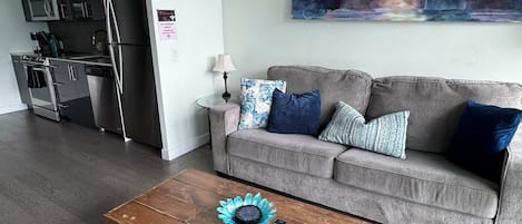 Una sala de estar moderna con un sofá gris, una mesa de centro de madera y un cuadro de un paisaje urbano en la pared.