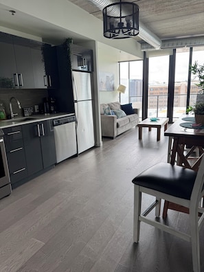 A modern kitchen with stainless steel appliances, a dining area with a table and chairs, and a large window offering a city view.