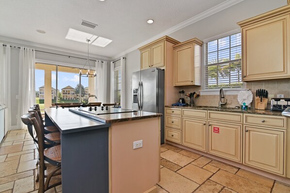 A modern kitchen with a central island, beige cabinetry, and a large window providing natural light.