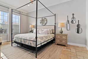 A four-poster canopy bed with a patterned bedspread, two bedside lamps, a wooden nightstand, and wall-mounted violin-shaped mirrors.