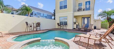 A two-story house with a swimming pool and hot tub, surrounded by patio furniture and palm trees.