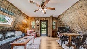 A cozy room with a ceiling fan, a sofa, a coffee table, a TV, and a dining area with chairs and a table.