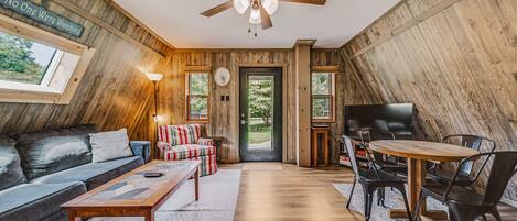A cozy room with a ceiling fan, a sofa, a coffee table, a TV, and a dining area with chairs and a table.
