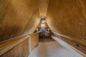 Ein schmales Schlafzimmer im Dachgeschoss mit Holzwänden, einer geneigten Decke, einem Bett mit Kopfteil und einem Deckenventilator.
