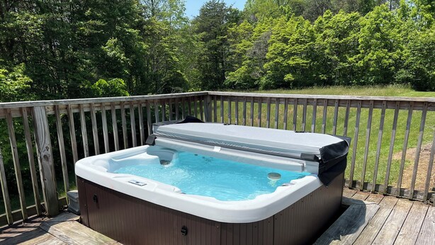A hot tub on a wooden deck with a wooden railing and trees in the background.