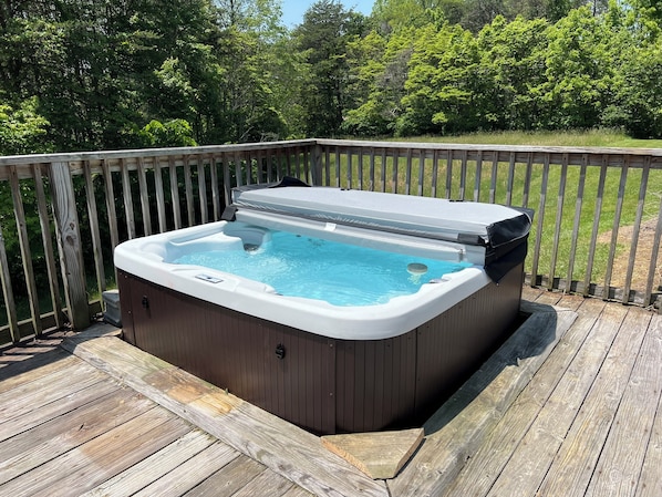 A hot tub on a wooden deck with a wooden railing and trees in the background.