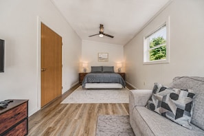 A bedroom with a bed, a ceiling fan, a window with a view, a wooden door, and a nightstand with a lamp. - Red Roost A-Frame - New Hot Tub (Rockbridge)