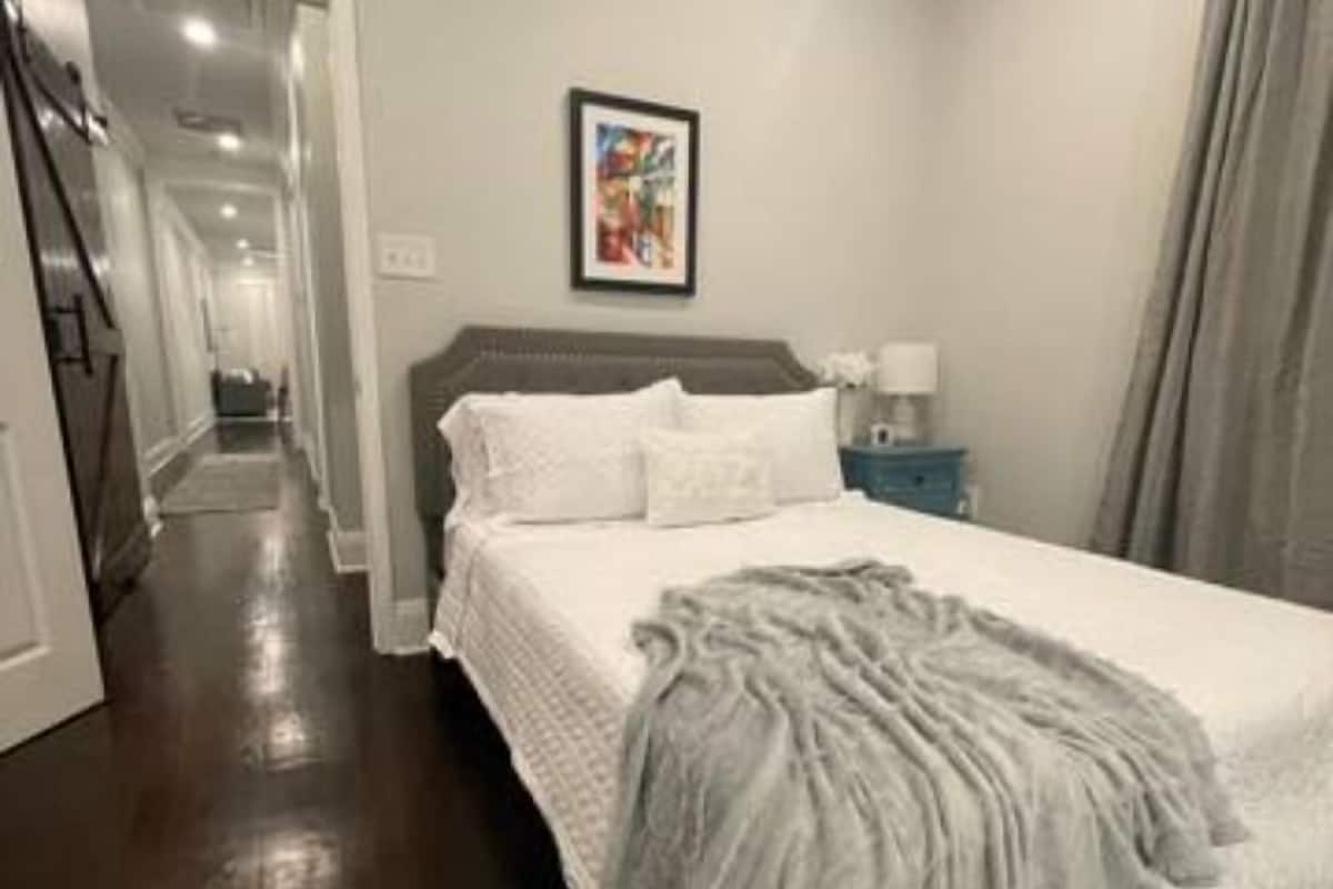 A bedroom with a large bed, a nightstand, a framed picture on the wall, and a hallway leading to another room.