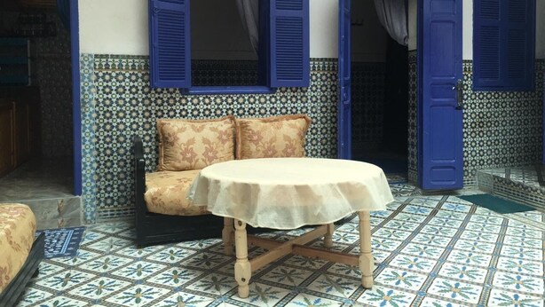 A room with a round table and a sofa, blue shutters, patterned tiles, and a doorway. - House (Marrakech)