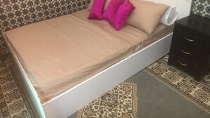 A bed with a beige mattress and pink pillows, a white headboard, and a dark nightstand with drawers. - House (Marrakech)