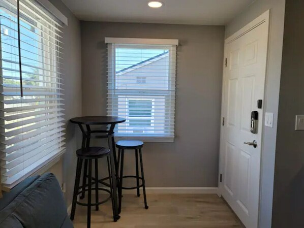 A small, narrow room with a window, a door, and a small table with two stools.