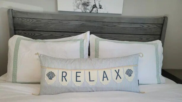 A bed with a pillow featuring the word "RELAX" and decorative shells. - Urban Oasis to Love, Near SF, Free Parking Onsite (Hayward)