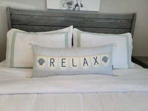 A bed with a pillow featuring the word "RELAX" and decorative shells.