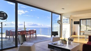 Een moderne woonkamer met een grote schuifglazen deur die uitkomt op een balkon met uitzicht op zee.