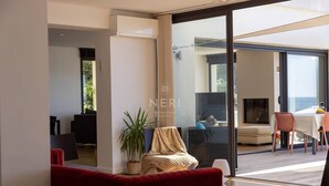 Een moderne woonkamer met een rode bank, een potplant en een glazen deur die leidt naar een balkon met een tafel en stoelen.