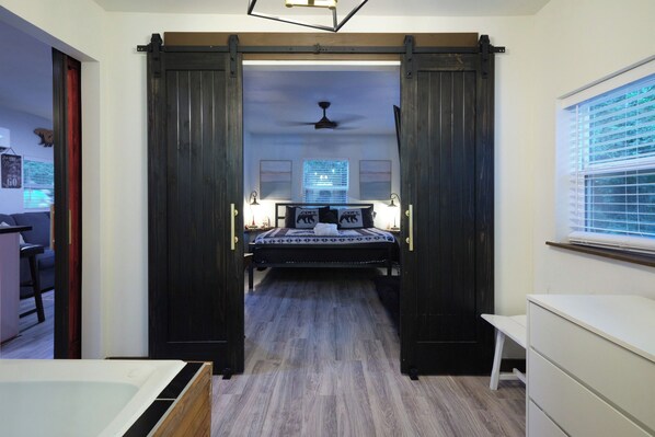 A bedroom with a bed, a ceiling fan, a window with blinds, and a door with a sliding mechanism.