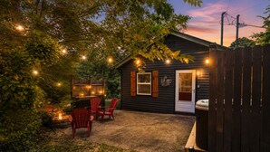 Une cabane en bois dotée d’un patio couvert, de chaises Adirondack rouges et de guirlandes lumineuses.