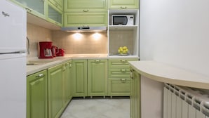 Una cocina con armarios verdes, un refrigerador blanco, un microondas y una cafetera.