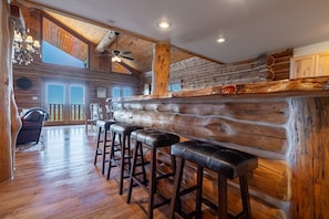 Interno di una baita di legno con angolo bar, pavimento in legno e una scala che conduce a un piano superiore.