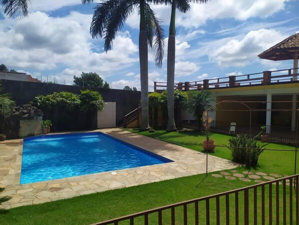 A swimming pool with stone tiles, surrounded by a well-maintained lawn and palm trees.