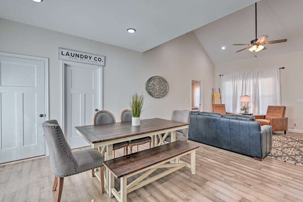 A dining area with a wooden table, grey upholstered chairs, and a bench. A ceiling fan and recessed lighting are visible.
