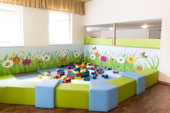 Un área de juegos infantiles con bloques de construcción de colores y un mural con flores e insectos en la pared.
