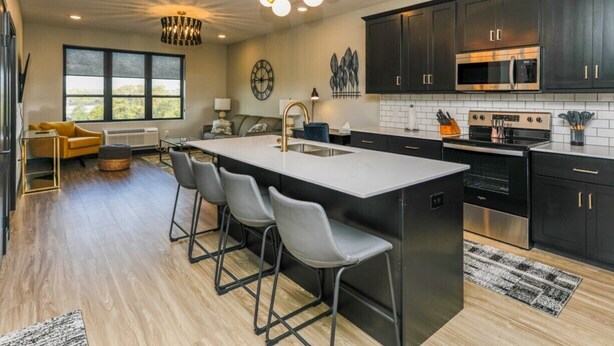 A modern kitchen with dark cabinets, stainless steel appliances, and a central island with bar stools. - The Fairway (Altoona)