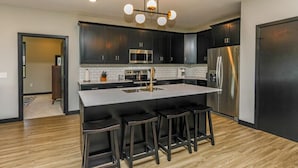 A modern kitchen with dark cabinetry, stainless steel appliances, and a central island with bar stools. - The Fairway (Altoona)