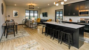 A modern kitchen with a central island, dark cabinetry, and a flat-screen TV mounted on the wall. - The Fairway (Altoona)