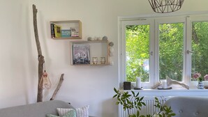A living room with a grey sofa, a wooden coffee table, a hanging light fixture, and a window with a view of greenery.