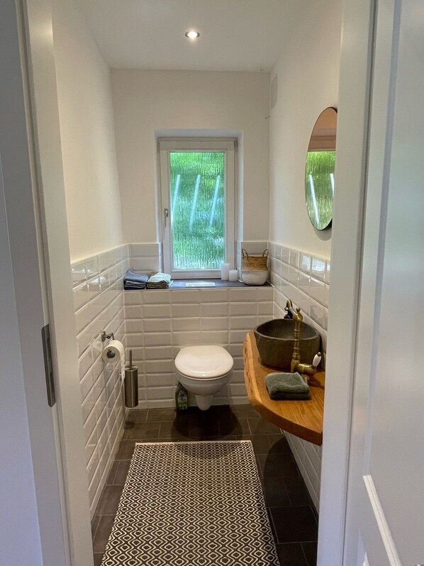 A compact bathroom with a toilet, a small window, and a wooden vanity with a sink.