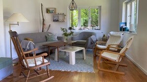 A living room with a sofa, two rocking chairs, a coffee table, and a lamp. There is a window with a view of greenery outside.