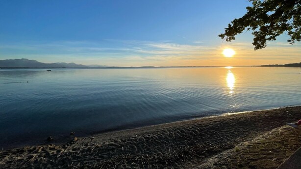 A calm lake at sunset with a clear sky and distant mountains.