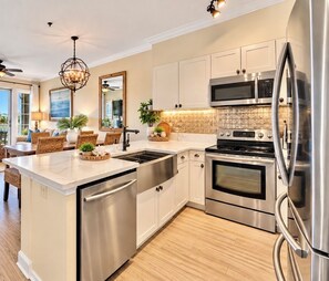 A modern kitchen with stainless steel appliances, a central island, and a view to the living area. - Coastal Comfort•On 30A•Between Rosemary Beach and Alys Beach•Three Bedroom• (Seacrest)
