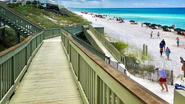 A wooden boardwalk leading to a beach with people and umbrellas. - Coastal Comfort,Spacious and Bright Condo right on 30A (Seacrest)